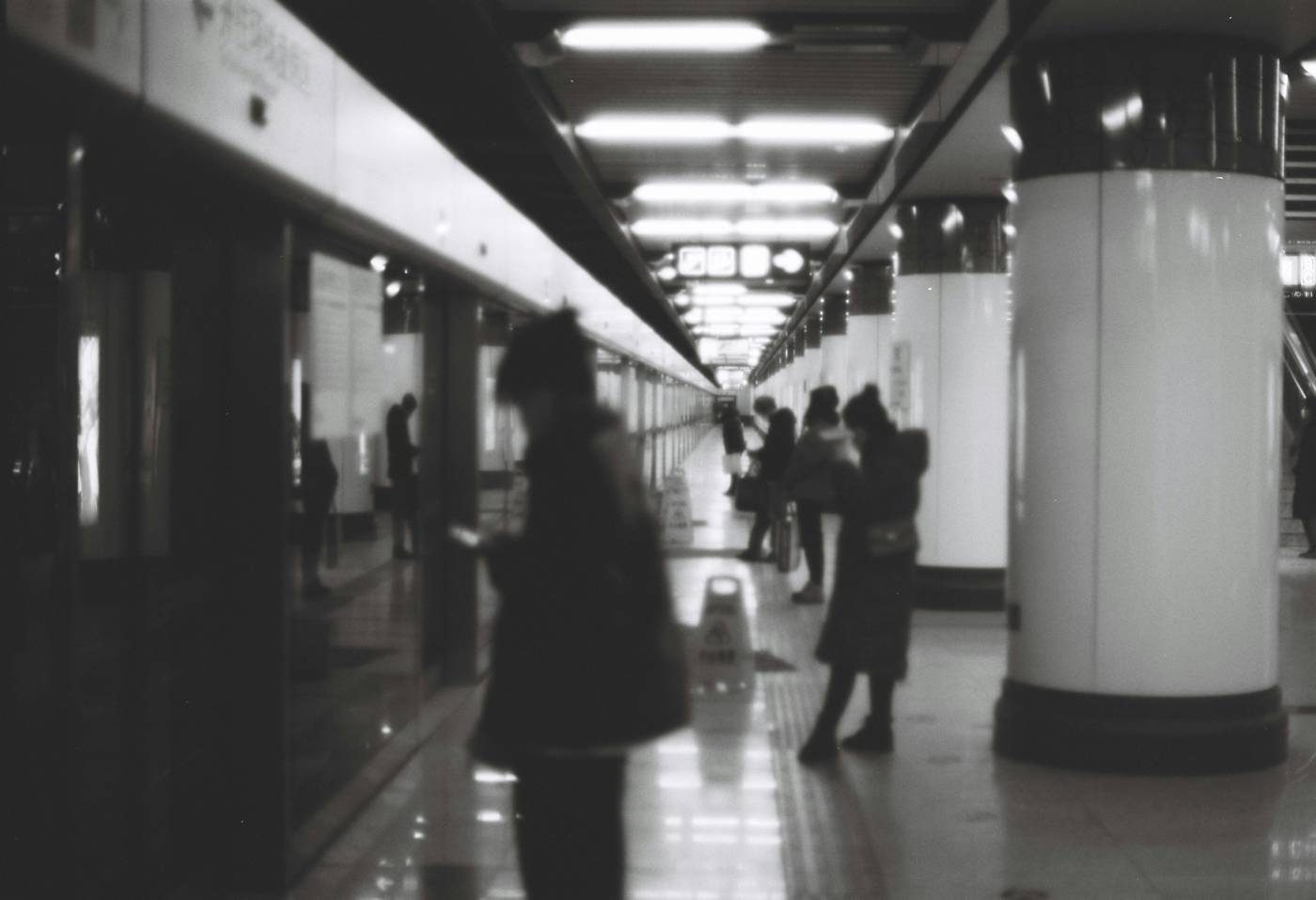 A transit platform receding into distance, figures spread along it