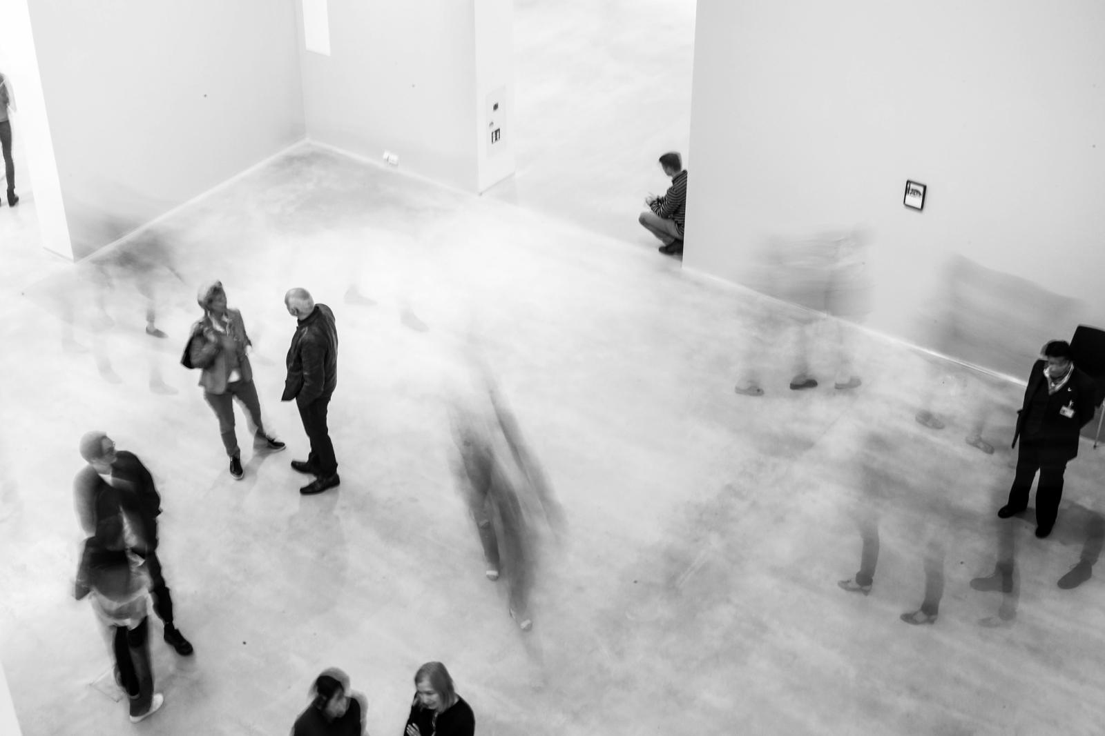 People scattered across a gallery, each alone in the same room